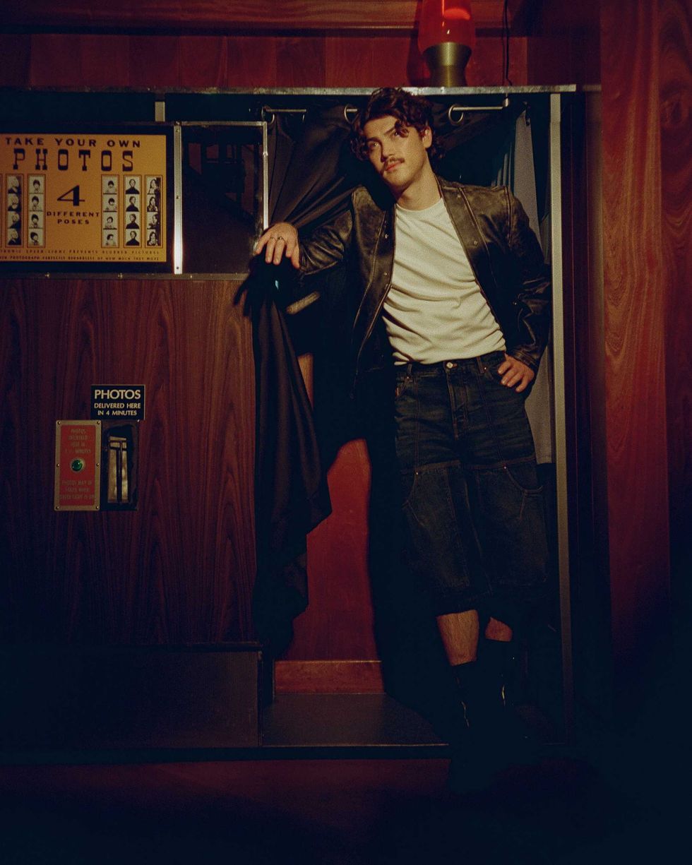 Jack Innanen in a white t-shirt, jean shorts, and leather jacket, standing in a Photo Booth.