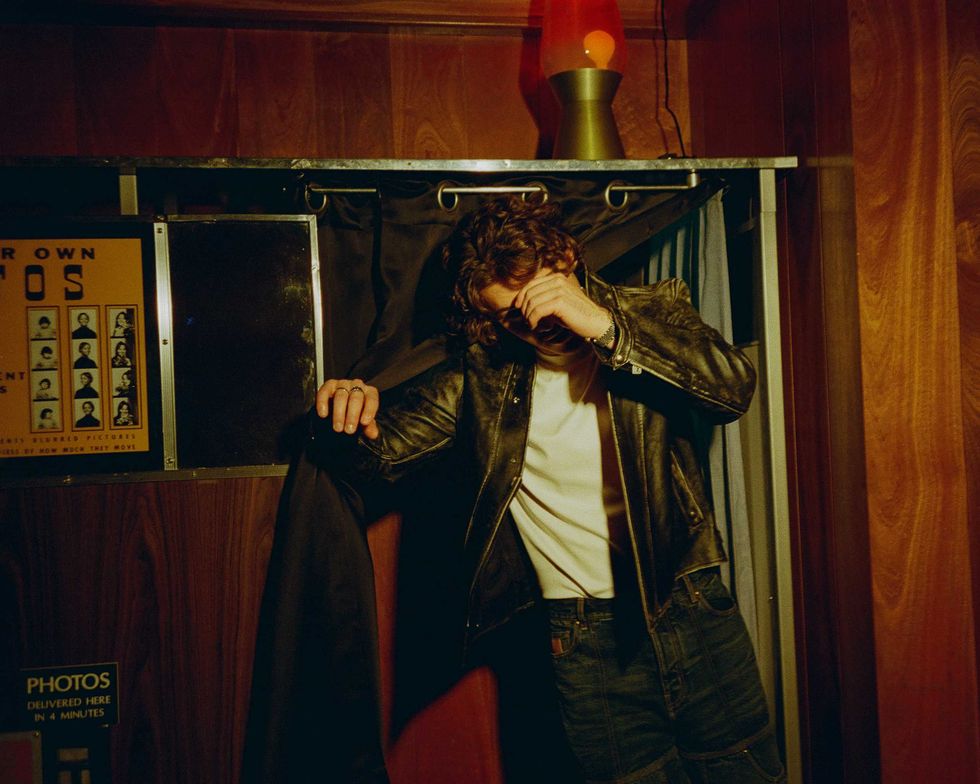 Jack Innanen in a white t-shirt, jean shorts, and leather jacket, standing in a Photo Booth.