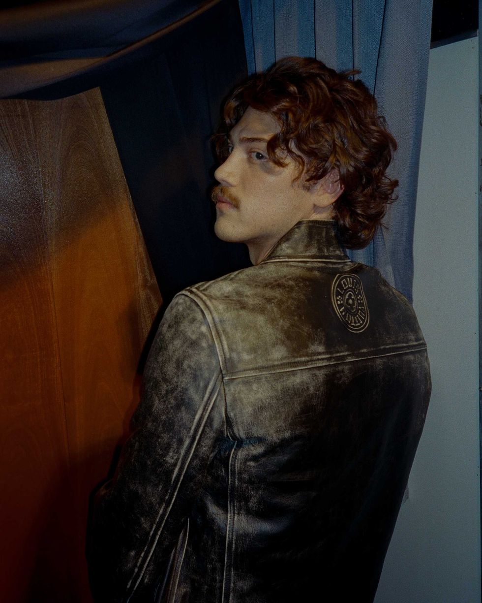 Jack Innanen in a white t-shirt, jean shorts, and leather jacket, standing in a Photo Booth.