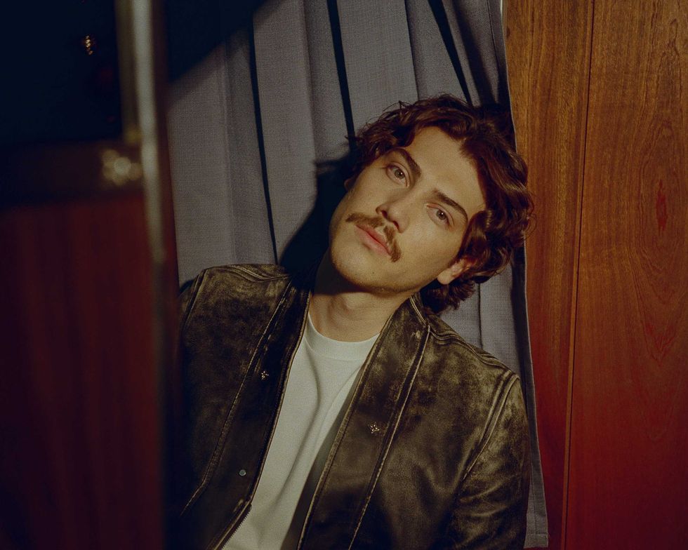 Jack Innanen in a white t-shirt, jean shorts, and leather jacket, standing in a Photo Booth.
